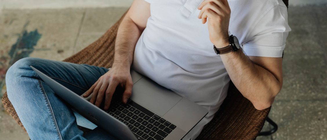 mężczyzna w białym t-shirt, w dżinsach z laptopem na kolanach